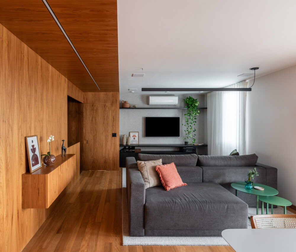 Sala integrada com madeira e sofá cinza em projeto da Labra
