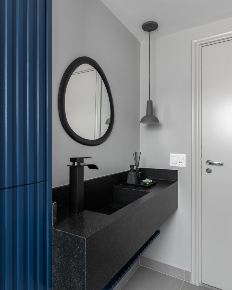 Lavabo com bancada escura e porta azul em projeto da Labra