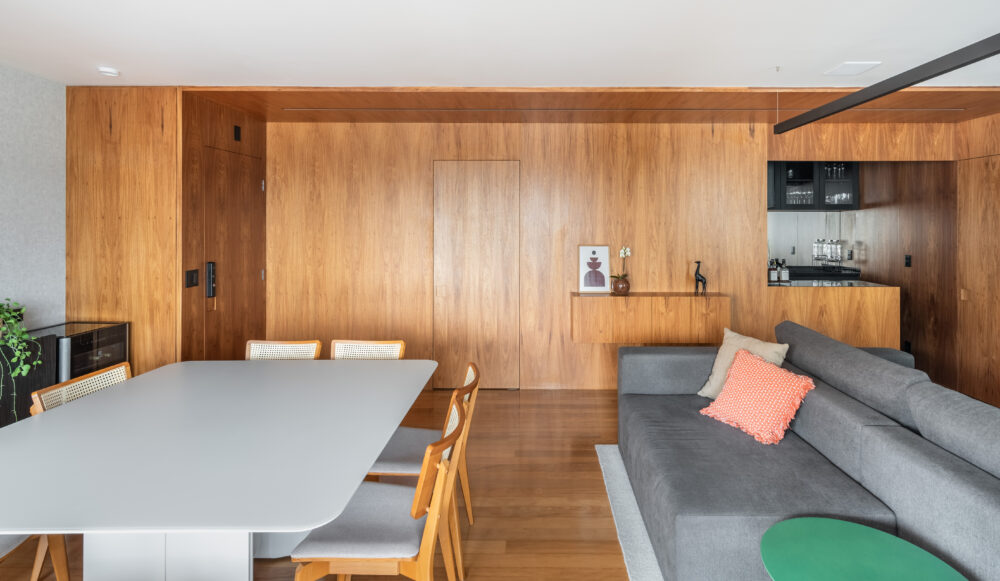 Estar integrado com bancada branca e painel de madeira em projeto da Labra