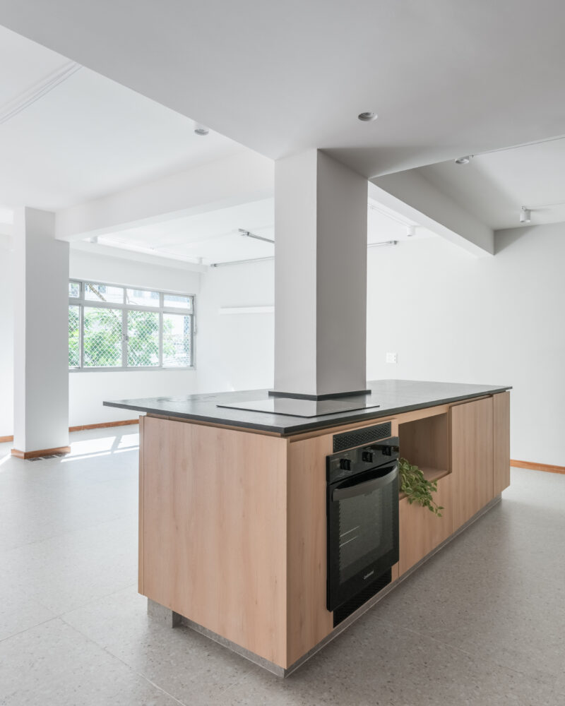 Cozinha integrada com bancada preta e marcenaria clara em projeto da Labra